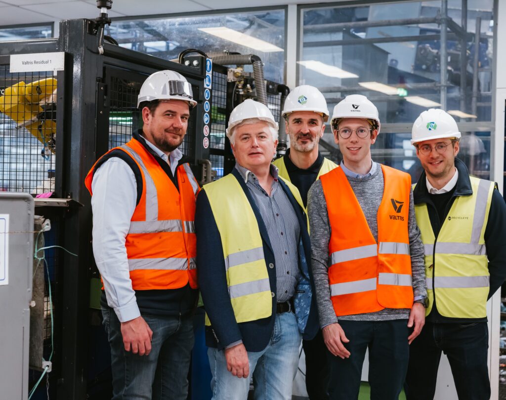 A group of men wearing protective clothing stand next to a robotic sorting installation